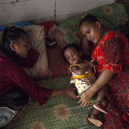 Photo of Rasminah resting on a mattress with two of her daughters.