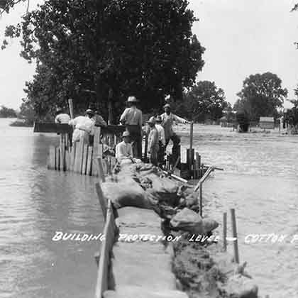 Archival black and white photo of men working on a levee with flood waters on both sides.