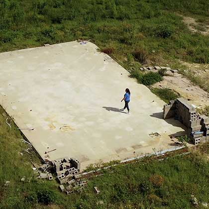 Drone photograph of Clair Marceaux standing on the concrete slab where her house used to be. 