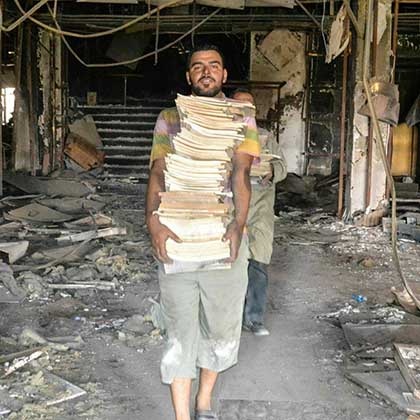 A volunteer carries dozens of books from inside Mosul University’s destroyed Central Library.