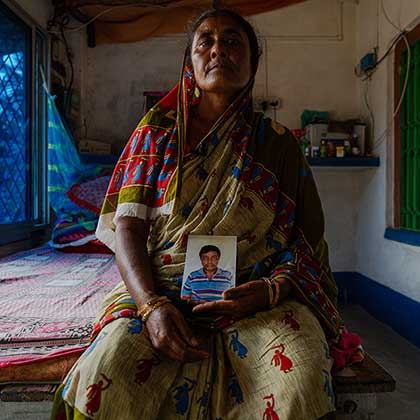 Portrait of a woman holding a photograph of her deceased husband in her lap.